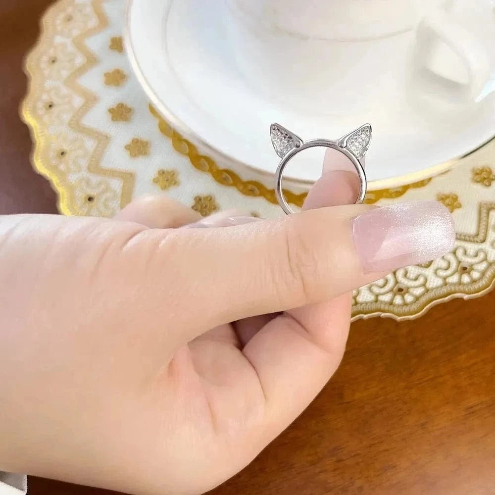 Hand wearing a silver ring with cat ears on a decorative plate with a teacup.