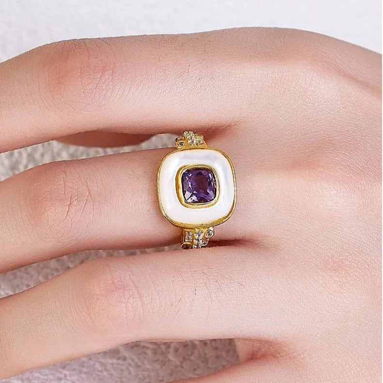 Gold ring with a purple gemstone on a finger against a neutral background