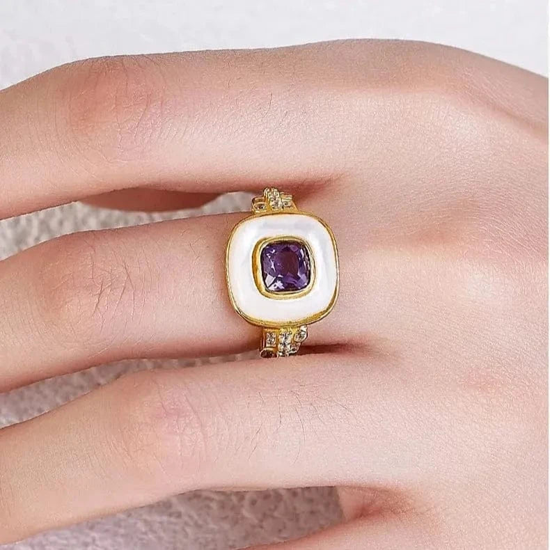 Gold ring with a purple gemstone on a finger against a neutral background
