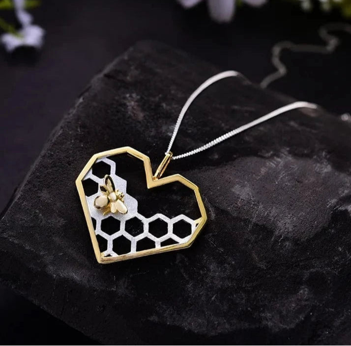 Heart-shaped gold and silver pendant with honeycomb design on a dark stone surface.