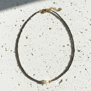 Necklace with black beads and a pearl-like clasp on a gray background