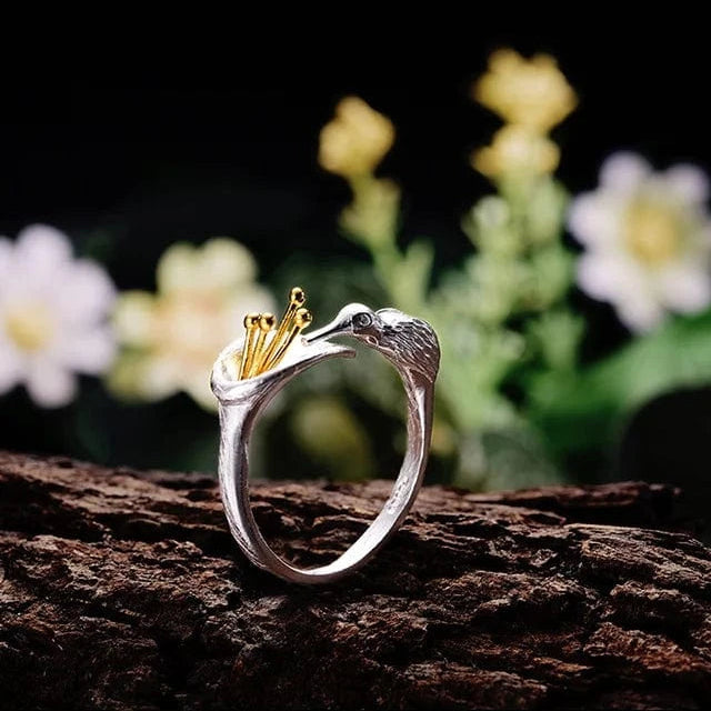 Silver ring with a gold crown on a wooden surface with flowers in the background