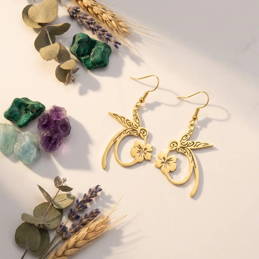 Gold earrings with floral designs on a light surface with decorative elements like leaves and stones.