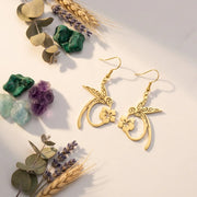 Gold earrings with floral designs on a light surface with decorative elements like leaves and stones.