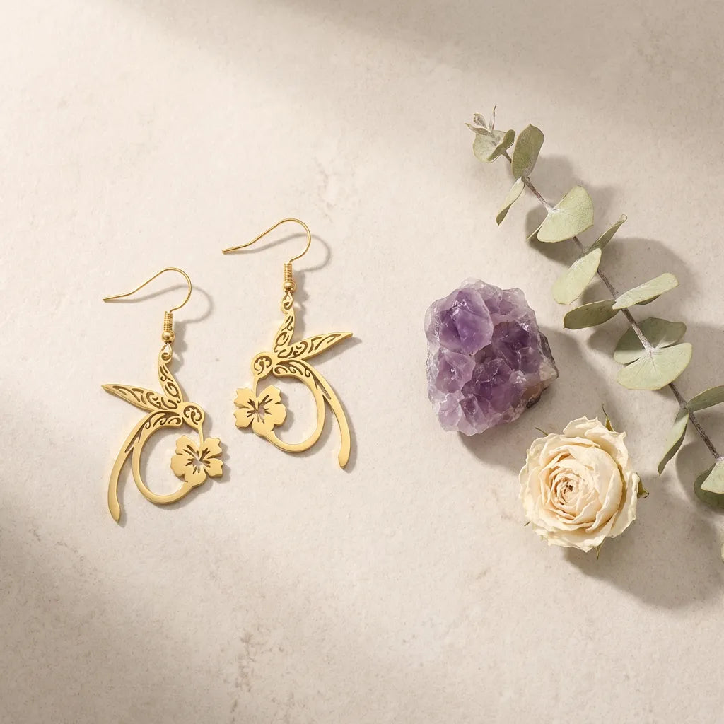 Gold earrings with floral designs on a beige surface with a purple crystal and white rose.