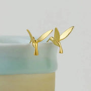 Gold hummingbird earrings on a light green background 
