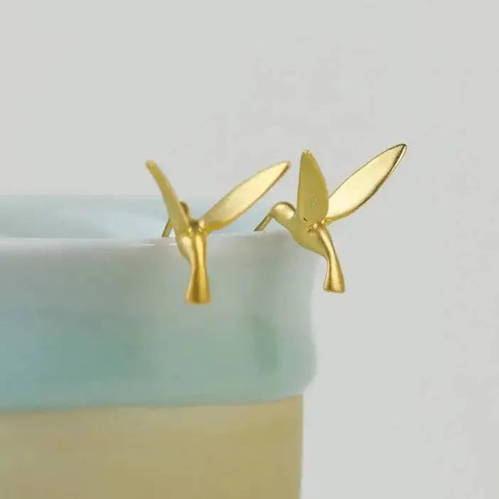 Gold hummingbird earrings on a light green background 