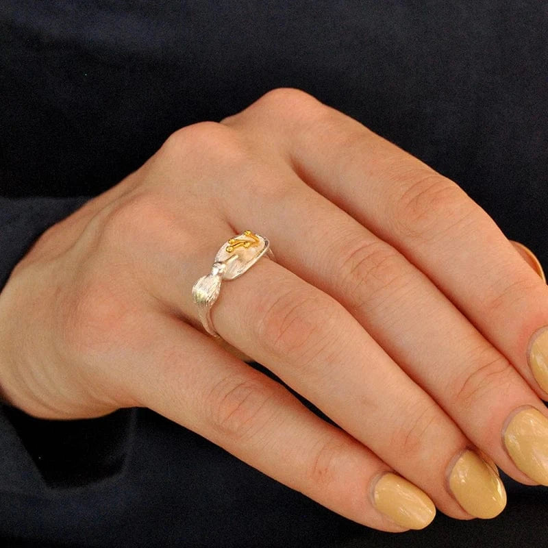 Hand wearing a gold ring with a yellow gemstone against a dark background