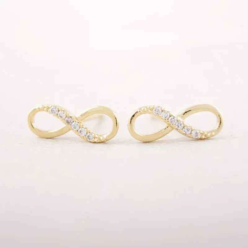 Gold infinity-shaped earrings with clear stones on a light gray background
