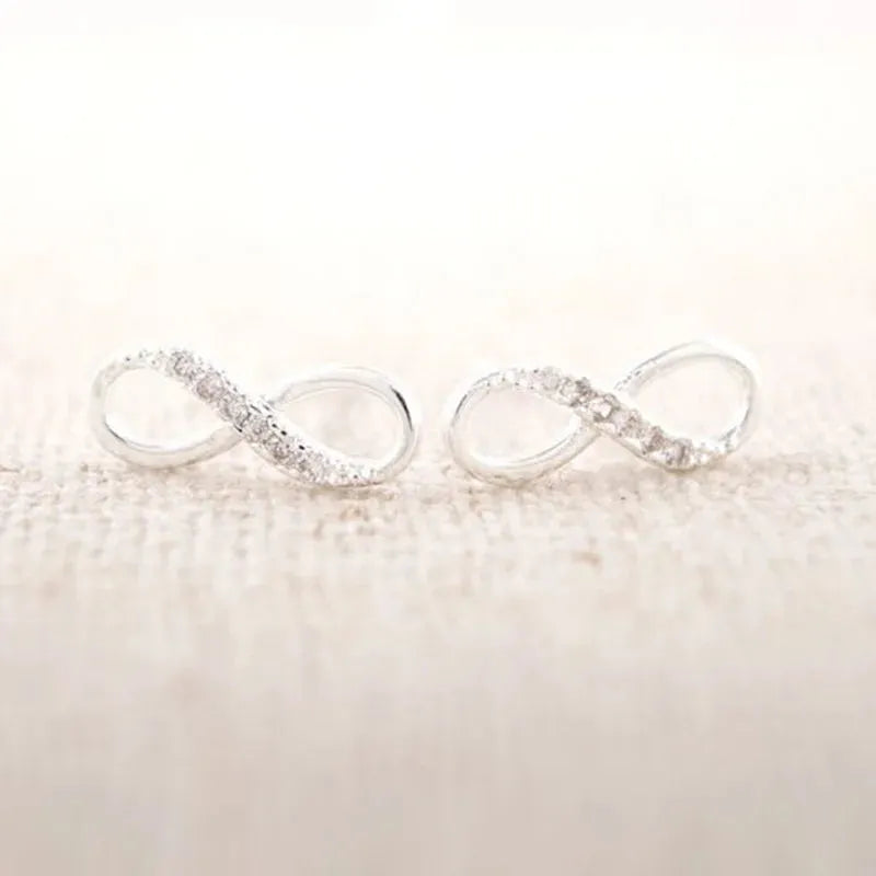 Two silver infinity ring earrings on a textured beige surface