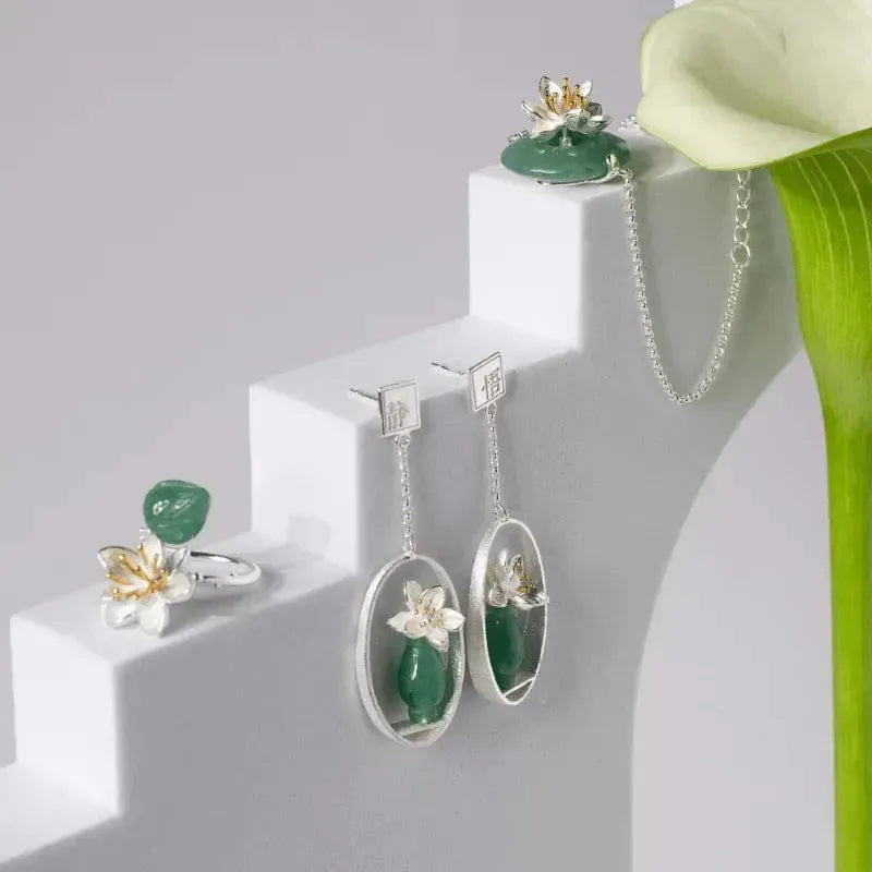 Jewelry set with green stones and silver accents on a white surface with a green flower.