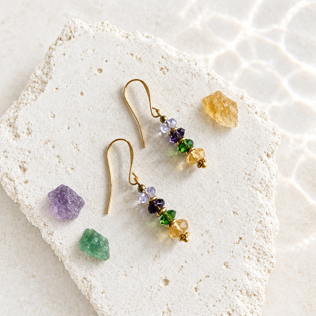 Pair of purple, green and yellow faceted glass drop earrings laid on a white stone