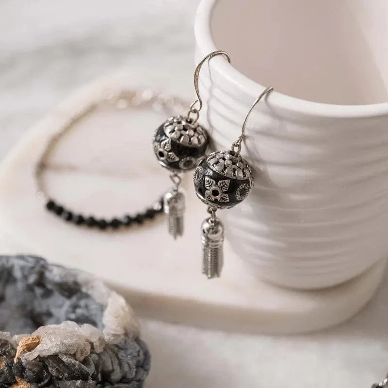 Silver earrings with black beads on a white surface with a cup and crystal rock.