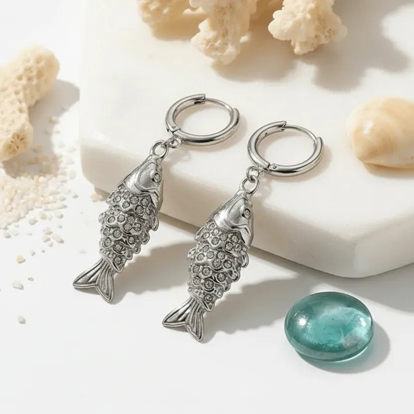 Pair of silver fish-shaped keychains on a light background with shells and a gemstone.