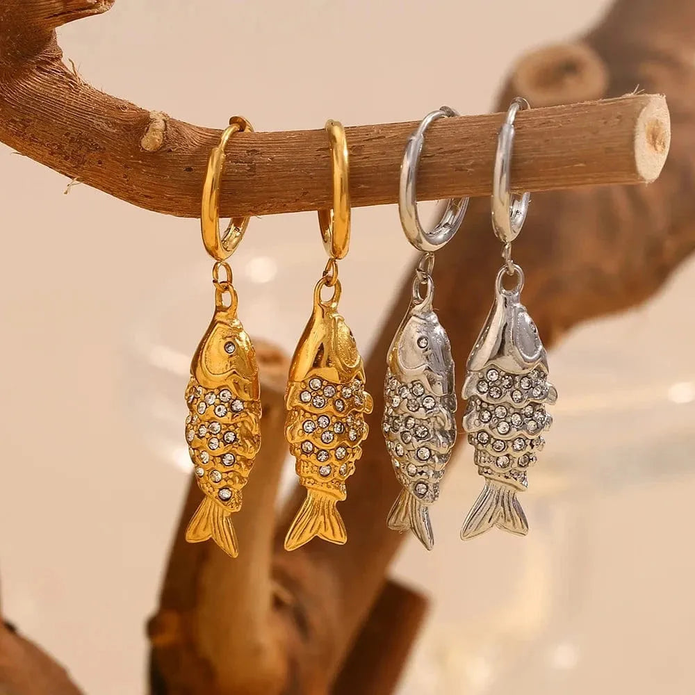 Gold and silver fish-shaped earrings hanging on a branch with a soft background.