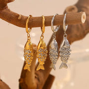 Gold and silver fish-shaped earrings hanging on a branch with a soft background.