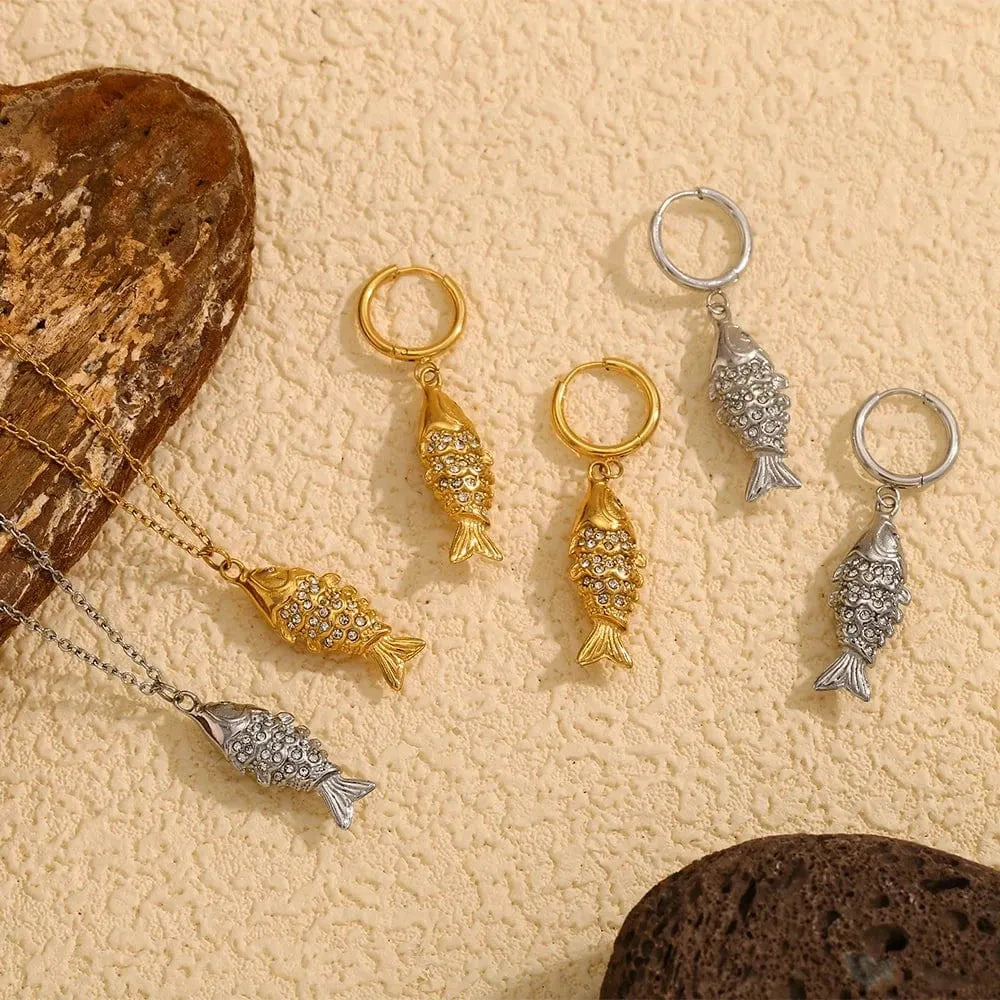Gold and silver fish-shaped keychains on a textured beige surface with rocks.