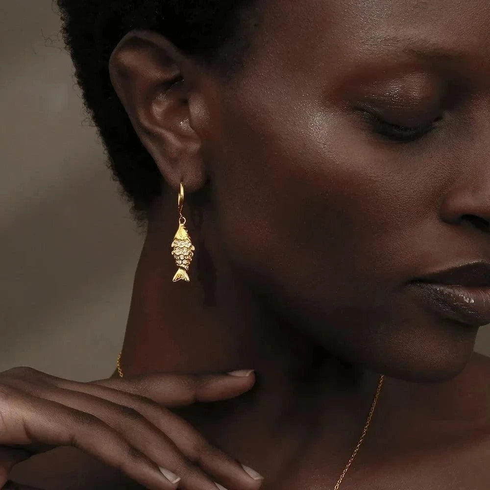 Close-up of a woman wearing gold earrings and a necklace against a neutral background