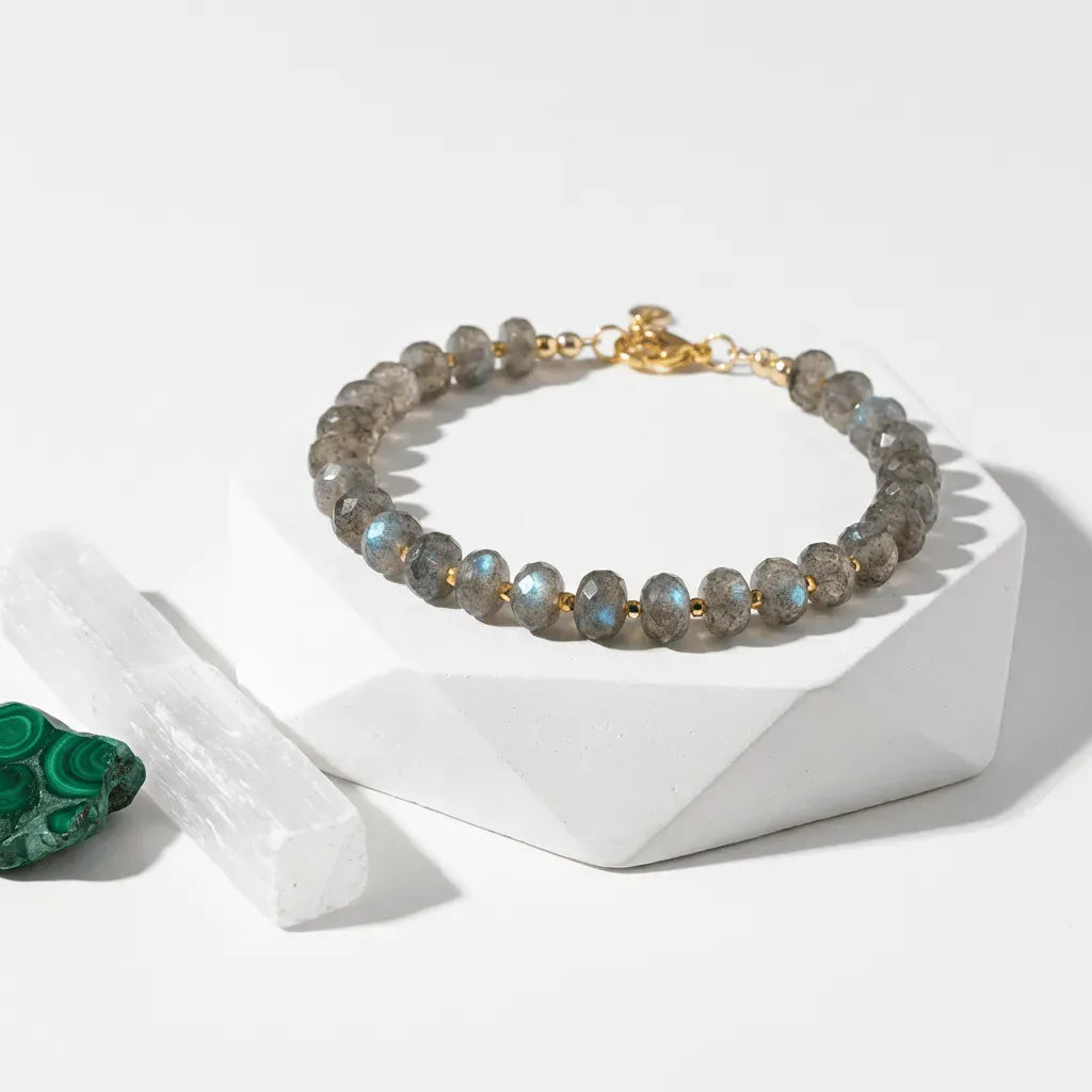 Bracelet with gray beads and gold accents on a white geometric stand