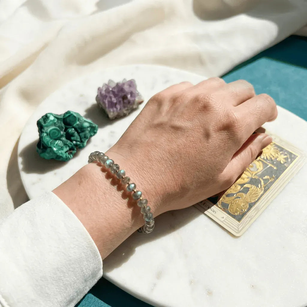 Hand wearing a bracelet with crystals and tarot cards on a marble surface