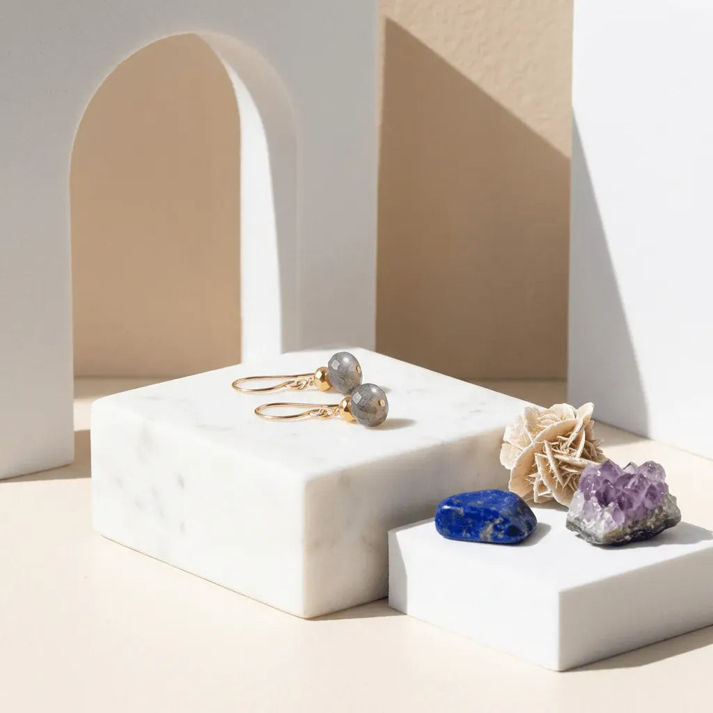Gold earrings on a white marble stand with decorative stones and a beige arch in the background