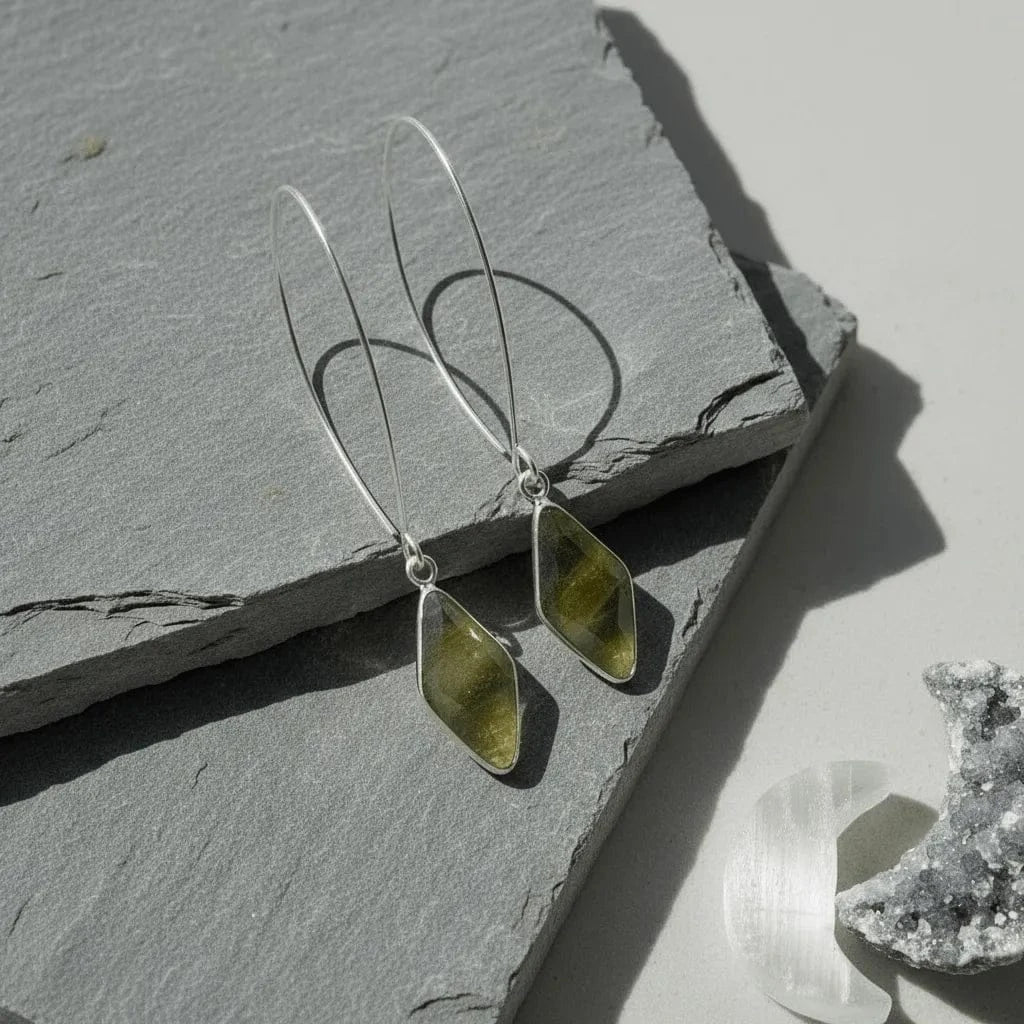 Silver earrings with green stones on a gray stone surface