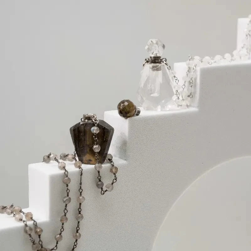 Necklaces and a small bottle on a white surface with a gray background