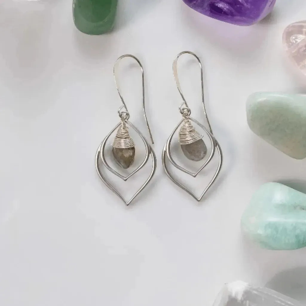 Silver teardrop-shaped earrings with gemstones on a white surface with stones around.