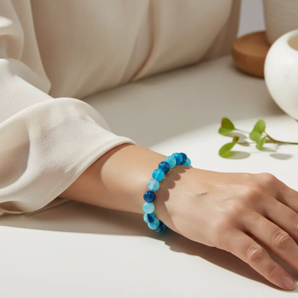 Hand wearing a blue beaded bracelet on a neutral background