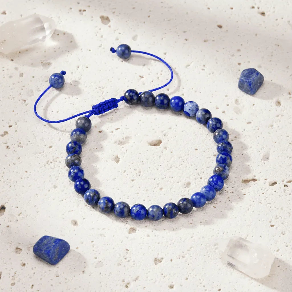 Blue beaded bracelet on a textured white surface with scattered lapis stones.