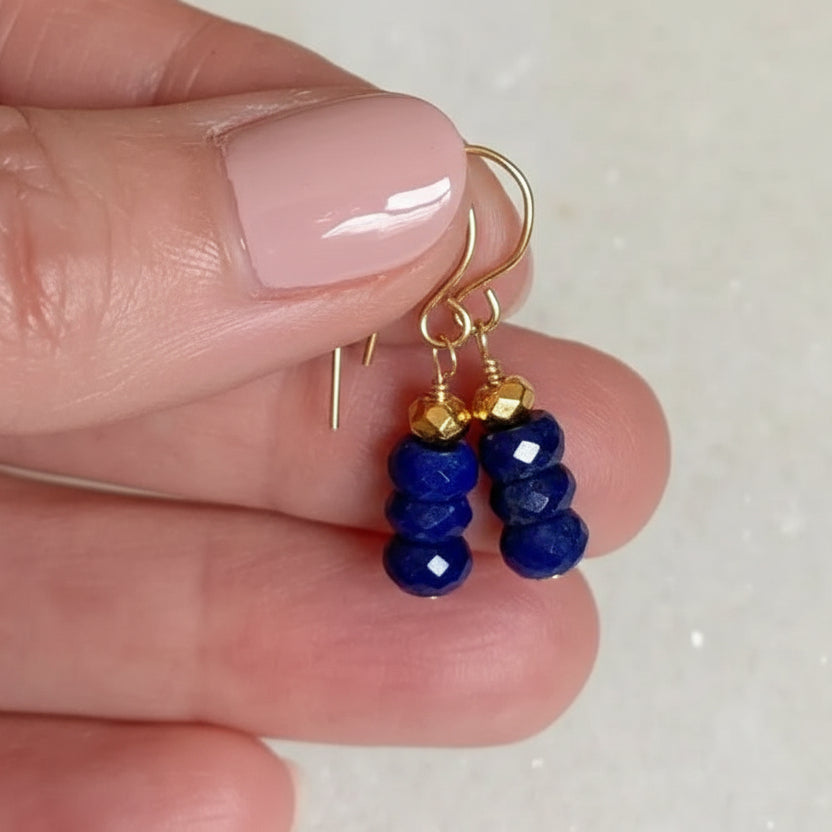 Gold earrings with blue beads held between fingers on a light background