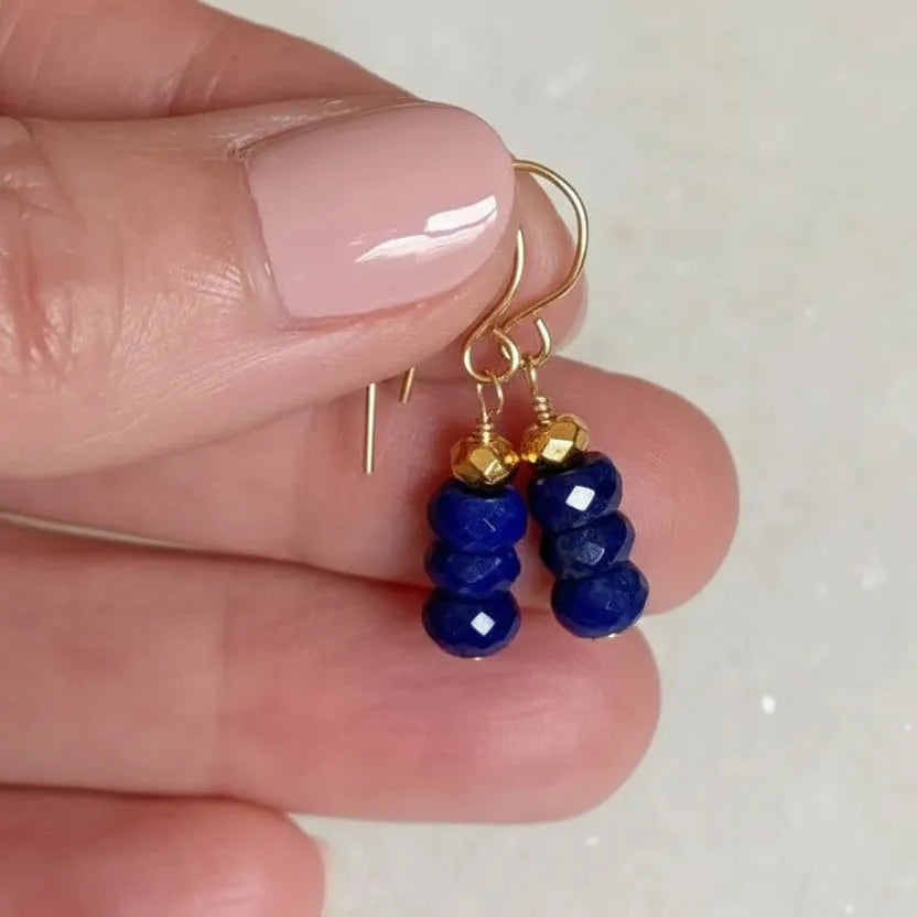 Gold earrings with blue beads held between fingers on a light background