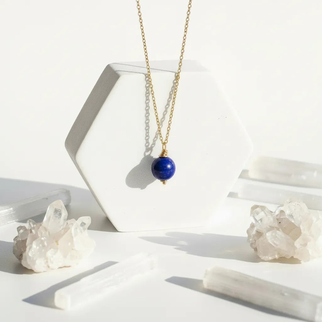 Gold necklace with a blue lapis lazuli pendant on a white surface with decorative stones