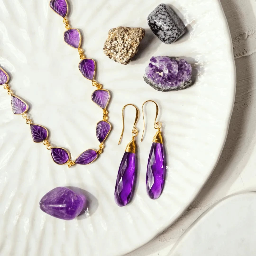 Purple jewelry set with necklace and earrings on a white surface with crystals.