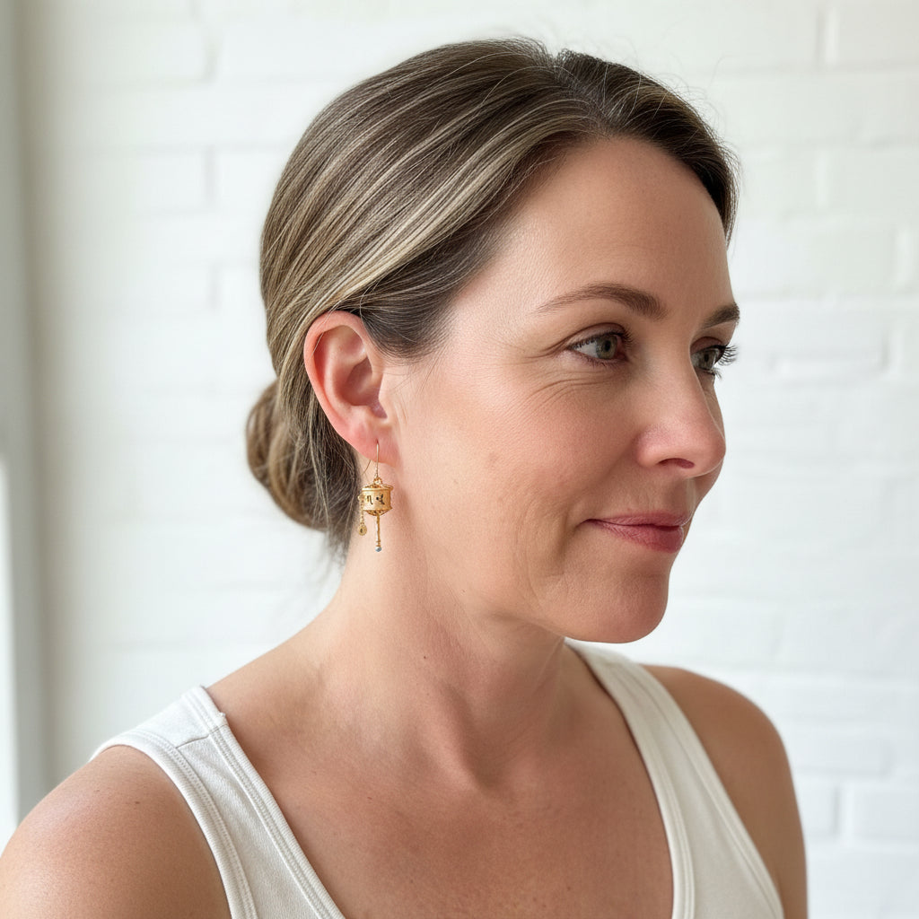 Woman wearing Tibetan prayer wheel drop earrings in sterling silver with 22k gold plating