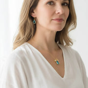 Woman wearing an aqua blue teardrop glass necklace and matching earrings in gold