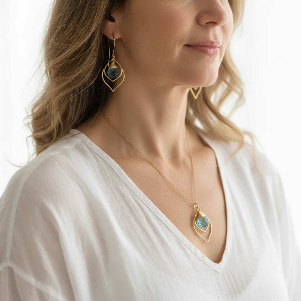 Woman wearing a gold blue topaz teardrop necklace with matching earrings, December birthstone jewelry