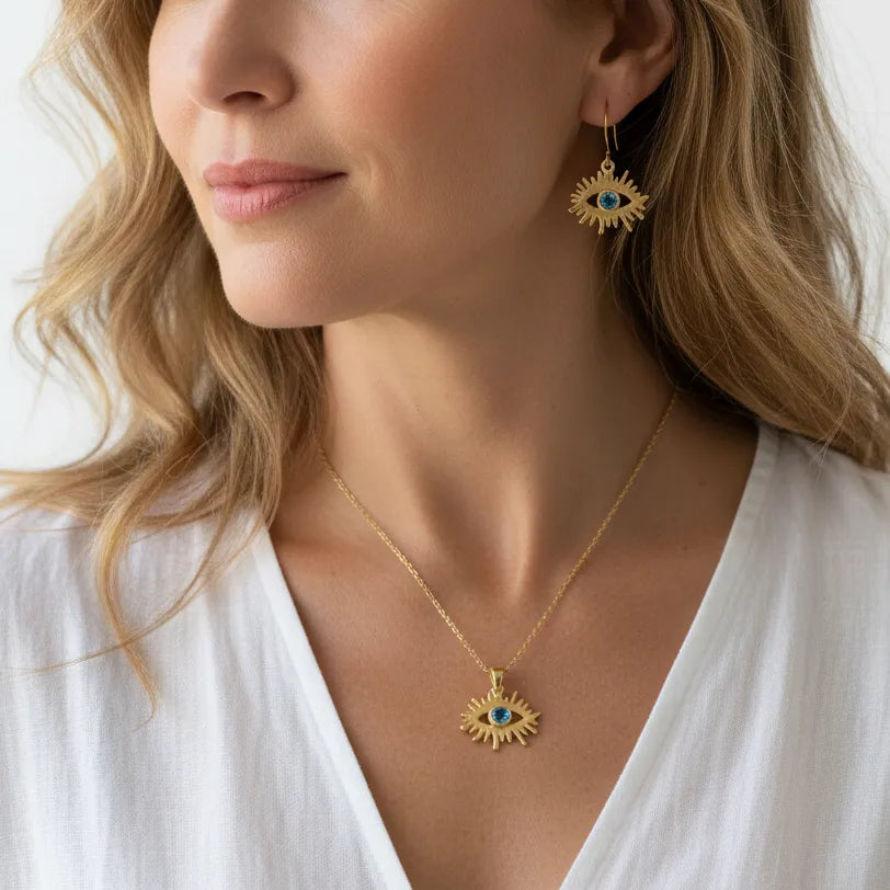 Woman wearing a blue topaz third eye necklace and earring set in gold, December birthstone jewelry