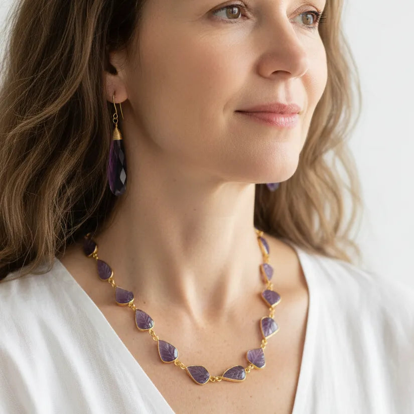 Woman wearing a carved amethyst chain necklace with statement drop earrings, February birthstone jewelry