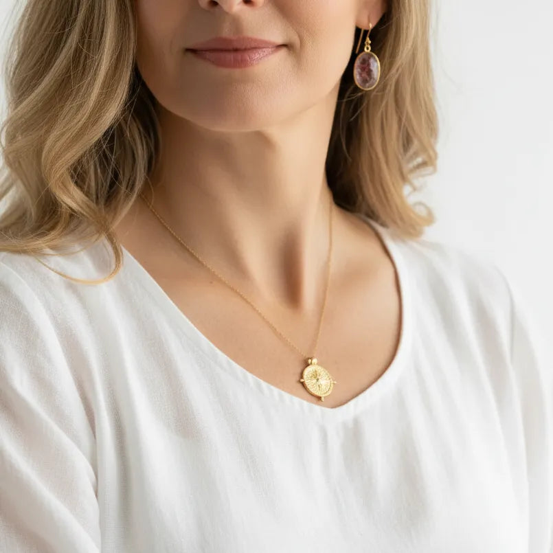 Woman wearing a compass medallion necklace with pink rutilated quartz drop earrings