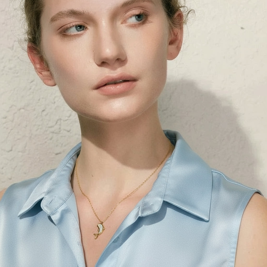 Woman wearing a black sleeveless top and gold necklace against a neutral background