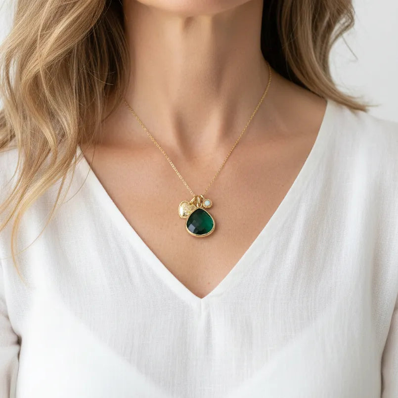 Woman wearing an emerald green charm necklace in gold, May birthstone jewelry