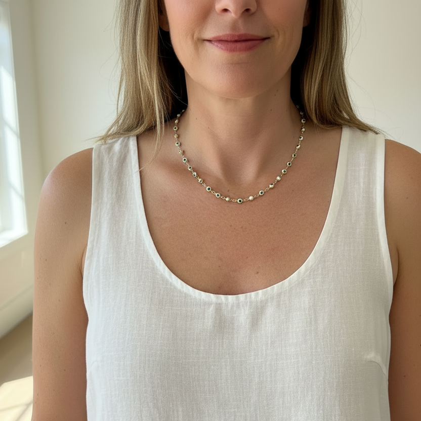 Woman wearing a short white and blue evil eye gold chain necklace at the collarbone
