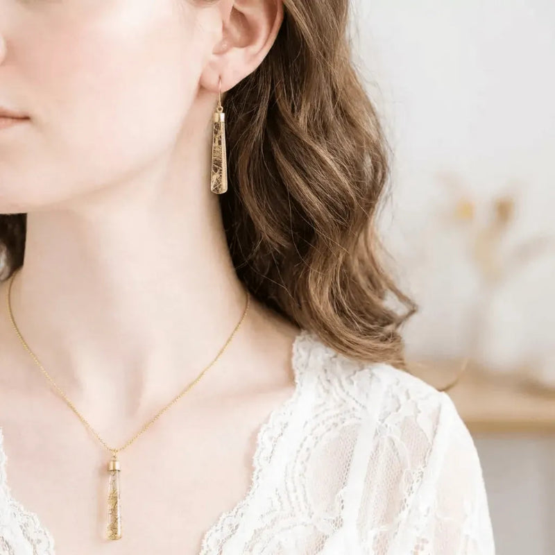 Woman wearing a golden rutilated quartz pendulum necklace and matching earrings in gold