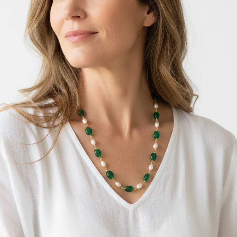 Woman wearing emerald green and pearl gemstone necklace in gold