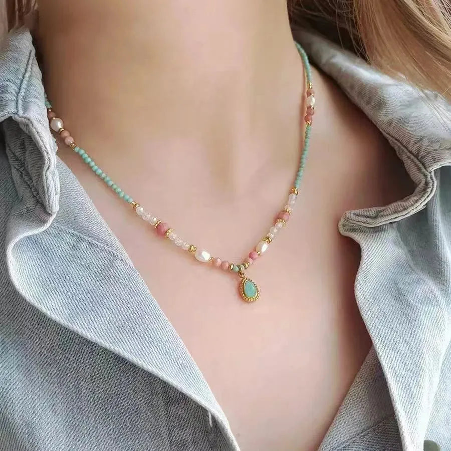 Necklace with colorful beads and a central pendant on a person wearing a light gray shirt.