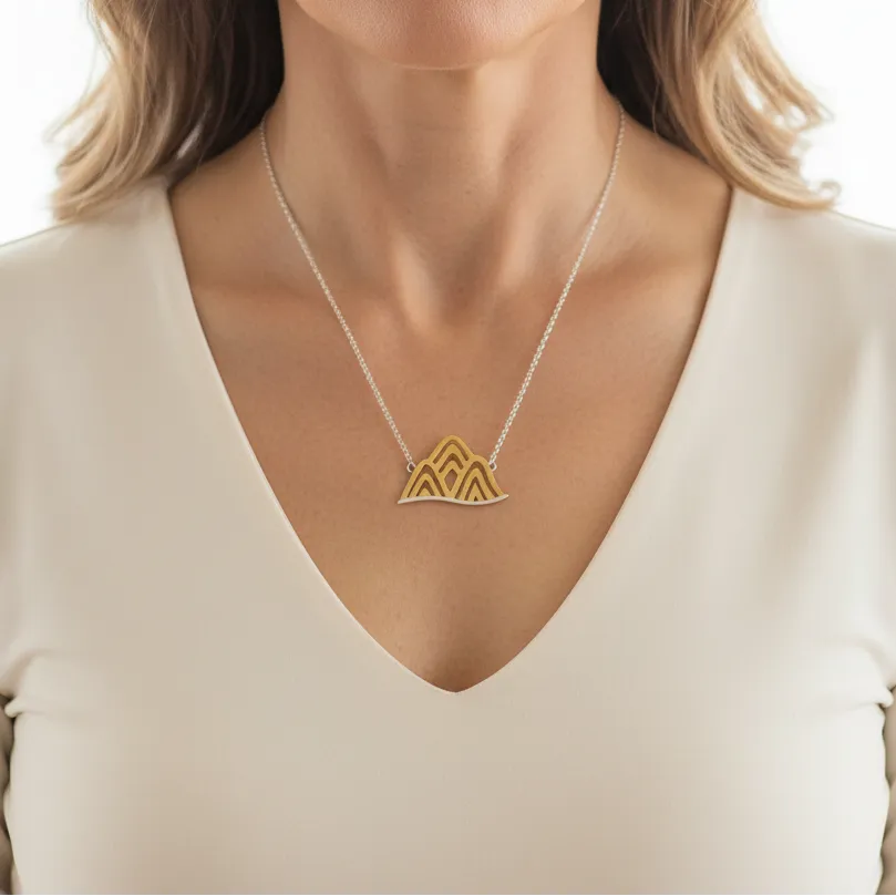 Woman wearing a mountain pendant necklace in gold and silver