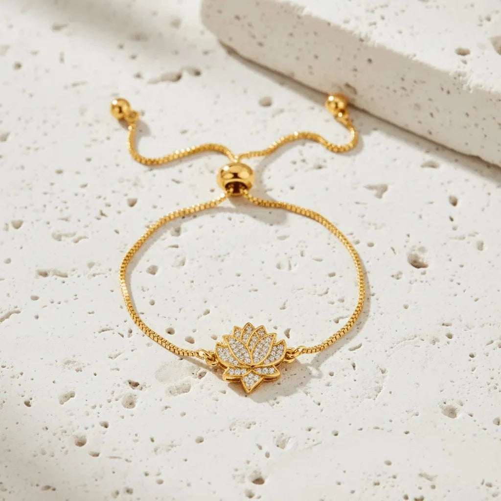 Gold bracelet with a lotus flower charm on a textured white surface
