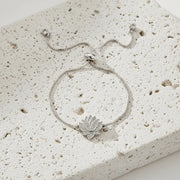 Silver bracelet with a lotus flower charm on a textured white surface