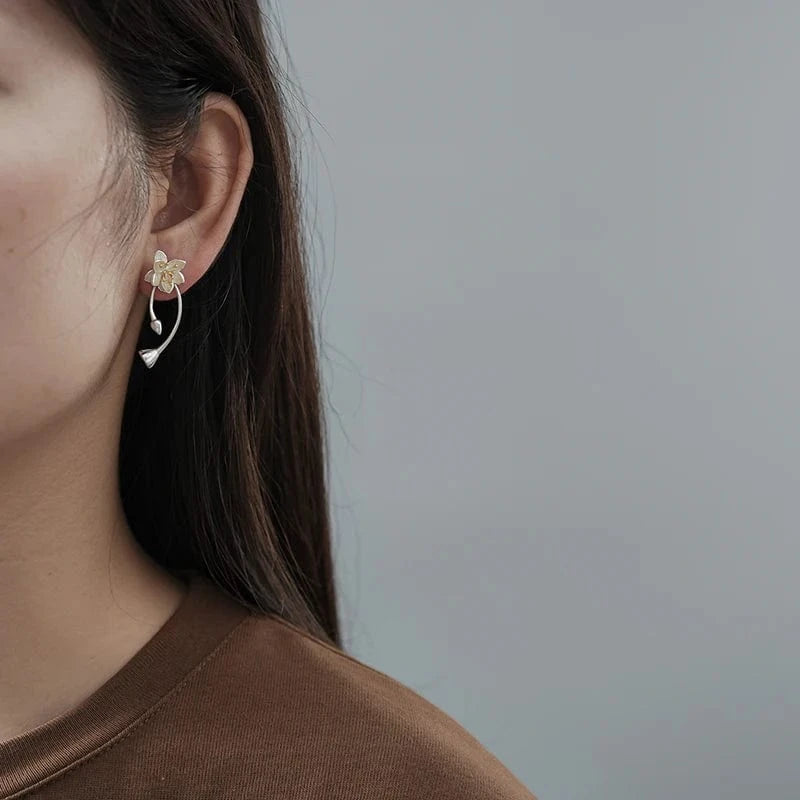 Close-up of a person wearing a delicate floral earring against a neutral background